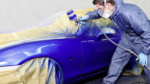 person in protective clothing painting a car with blue paint person in protective clothing painting a car with blue paint